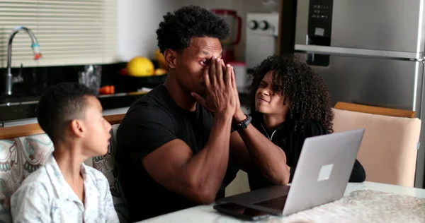 Black father working at home while children interrupt and complain