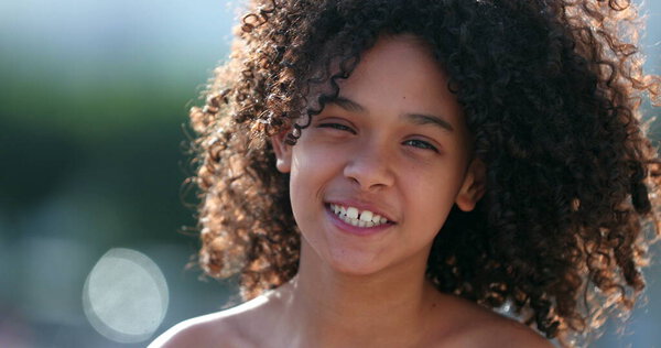 Black preteen girl child smiling at camera standing outside. African kid with curly hair