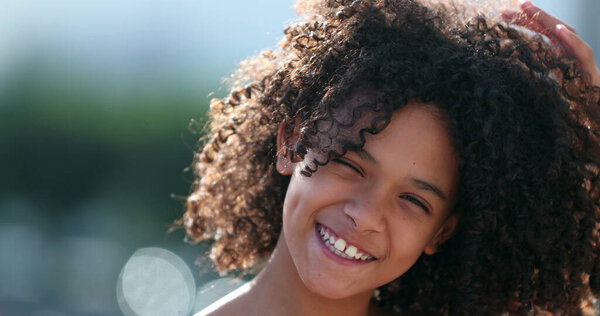 Black preteen girl child smiling at camera standing outside. African kid with curly hair