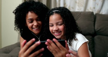 İki genç kız cep telefonu ekranında eğlence medyasına heyecanla tepki veriyor.