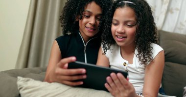 Evde akıllı telefon kullanan iki küçük kız. Genç arkadaşlar akıllı telefon ekranını paylaşıyor