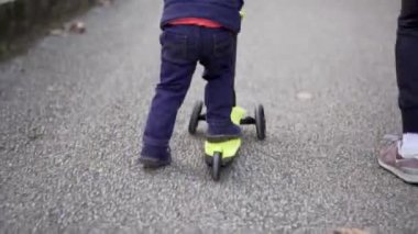 Küçük çocuk parkta üç tekerlekli oyuncak scooter kullanıyor.