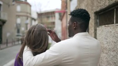 Afrikalı bir adam şehir kaldırımında yürürken kız arkadaşını okşuyor.