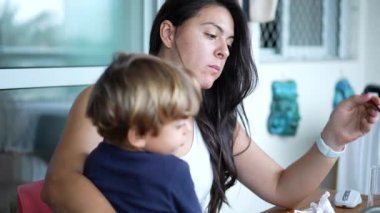 Anne kucağında çocukla yemek yiyor. Annesi küçük çocuğu çatalla besliyor..