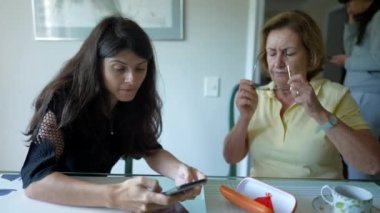 İki kişi cep telefonu ekranına bakıyor. Yaşlı kadın okuma gözlüğü takıyor. Üst düzey anneyle internet paylaşımı ekranı taraması.
