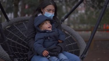 Anne covid-19 yüz maskesi takıyor, yeni yürümeye başlayan oğluyla salıncakta sallanıyor, anne ölüm anında kaynaşıyor.