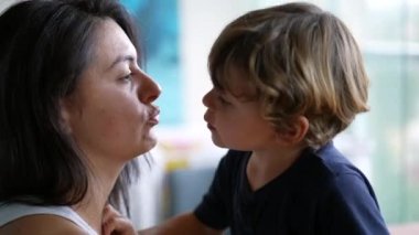 Küçük çocuk annesini yanaklarından öpüyor. Annesine sevgi ve şefkat gösteren bir çocuk. Küçük çocuk ebeveyni öpüyor..