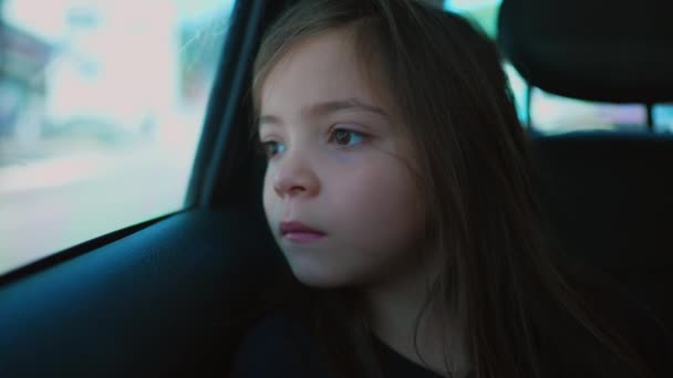車の後部座席の小さな女の子 車の窓の外を見ている一人の思慮深い子供のクローズアップ顔がぼんやりと — ストック動画