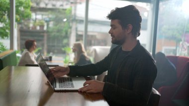 Genç girişimci ya da işçi, kahve dükkanında uzaktan çalışan dizüstü bilgisayar açıyor.