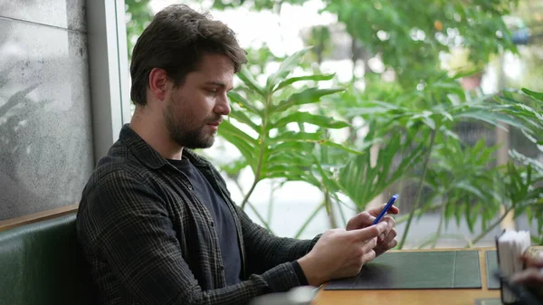남자가 온라인에서 창문을 커피숍에 있습니다 스마트폰으로 내용을 읽으면서 말하는 — 스톡 사진