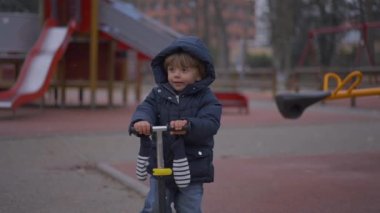 Küçük çocuk kış boyunca parkta dikilip scooter 'ı tutuyor.