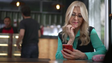 Üst düzey yönetici kadın kahve dükkanında akıllı telefon kullanıyor. Kafe restoranında İnternet 'te gezinen kararsız yaşlı kişi