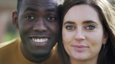 Afrikalı adam ve beyaz kız yüzleri kameraya bakıp gülümsüyor.