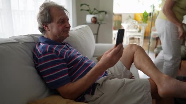 拿着手机的老年人用智能手机用视频讲话 在客厅沙发上使用现代技术设备的老实人 — 图库视频影像