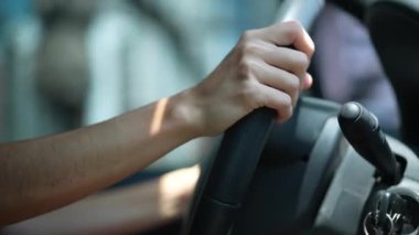 Sürücü elleri direksiyonlu arabayı yolda tutuyor. Direksiyondaki kişinin eli yakındır. Araç kullanan bir kadın. İşten işe giderken.