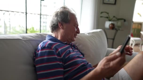 一位快乐的老人坐在客厅的沙发上与家人在手机上交谈时笑逐颜开 — 图库视频影像