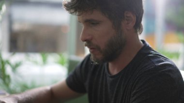 Genç adam kahve dükkanında oturan dizüstü bilgisayarını kullanarak internette geziniyor. Çevrimiçi arama klavyesinde bilgisayar ekranına bakan kişi