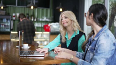 Kahve dükkanında dizüstü bilgisayarın önünde iki kadın. Kafe 'de uzaktan çalışan yeni kadın işçiye üst düzey yönetici yönelimi