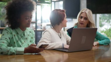 Kahve dükkanında dizüstü bilgisayarın önünde oturan üç farklı kadın. Genç çalışanlar ve yönetici kadın çalışanlar.
