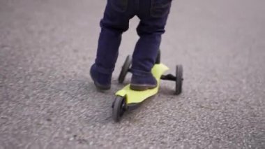 Küçük çocuk parkta üç tekerlekli oyuncak scooter kullanıyor.