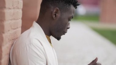 Dışarıda oturan siyah bir adam bilgisayarda yazı yazıyor. Afrikalı kişi uzaktan çalışma