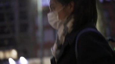 30 'lu yaşlarda bir kadın gece kaldırımda yürürken maske takıyor.