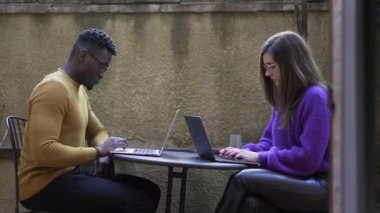 Evde bilgisayar başında çalışan insanlar var. Afrikalı erkek ve genç beyaz kadın birlikte.