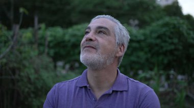 Meditative older man standing outside at park looking at sky in contemplation