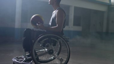 Tekerlekli sandalyedeki engelli atlet elinde tutuş topuyla spor elbise giyiyor.