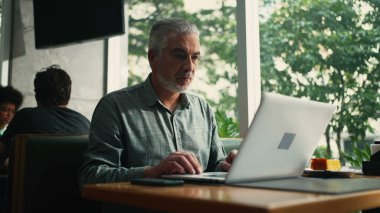 Kafe mağazasında oturan eski yönetici bilgisayarı uzaktan çalıştırıyor. Orta yaşlı bir adam internetten kafeteryadaki bilgisayarla internette geziniyor.