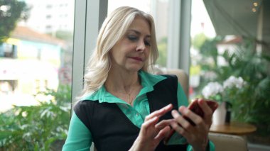 Kahve dükkanında telefonu kullanan yaşlı bir kadın. Üst düzey iş kadını kafeteryadaki akıllı telefondan mesaj yazıyor. Cep telefonuna bakan kadın yönetici