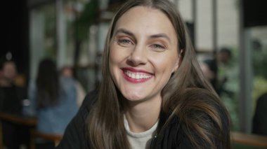 Kahve dükkanında oturan ve kameraya gülümseyen genç bir kadının portresi. 20 'li yaşlardaki mutlu kız gülümsüyor