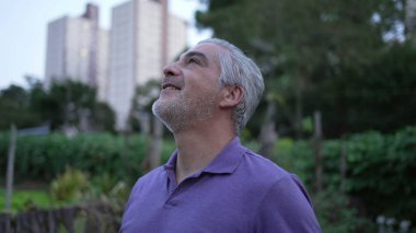 Contemplative older man looking up in meditation and peace. Senior person having HOPE opening eyes to sky in the evening