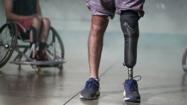 Protez bacaklı engelli biri. Arka planda tekerlekli sandalyedeki biri var. Azim ve motivasyon kavramı