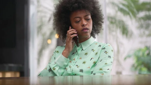 African American woman making a phone call with cellphone. A black girl seated at coffee shop speaking on smartphone device