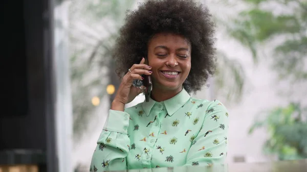 African American woman making a phone call with cellphone. A black girl seated at coffee shop speaking on smartphone device