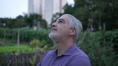 Meditative older man standing outside at park looking at sky in contemplation