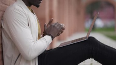 Genç siyahi adam dışarıda dizüstü bilgisayarla uzaktan çalışıyor. Bilgisayarda yazan Afrikalı girişimci veya öğrenci