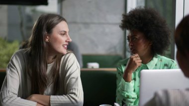 Kahve dükkanındaki çeşitli kadınlar muhabbet ederken. Kafede oturmuş gülen dizüstü bilgisayarlı üç kız arkadaş grubu.