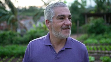 Contemplative senior man walking outdoors in small farm. Pensive older person walks forward portrait face closeup