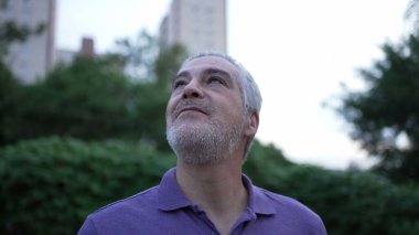 Contemplative older man looking up in meditation and peace. Senior person having HOPE opening eyes to sky in the evening