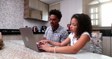 Brezilyalı baba ev mutfağında kızına dizüstü bilgisayarda yardım ediyor.