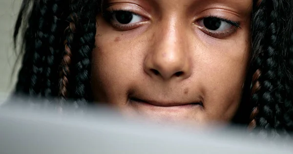 Close-up girl face looking at computer screen. Child staring at laptop browsing internet