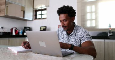 Ev mutfak masasında dizüstü bilgisayar kullanan odaklanmış bir Afrikalı.