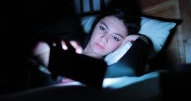 Genç kadın ile smartphone yatakta. Yatmadan önce cep telefonu cihaz oynadığı kadın 