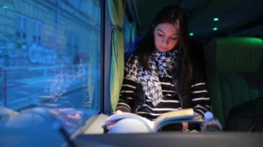 Akşamları otobüsle seyahat eden bir kadın. Hareket halindeyken kitap okuyan kız