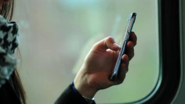 Trenle gidip gelirken akıllı telefonu tutan eller. E- postaları kontrol eden ve cep telefonu aygıtıyla internette gezinen kişi