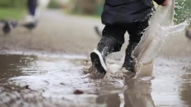 Yağmur botlarıyla su birikintisinde koşan bir çocuk