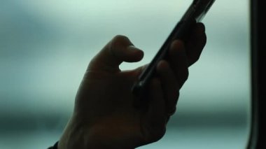 Hareket halindeki bir trende cep telefonu cihazını tutan kişinin yakın çekimi. Bulanık arkaplan hareket halinde.