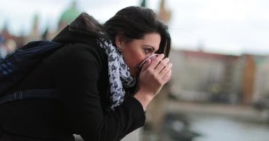 Köprüde dalgın dalgın yatarken sıcak bir içecek yudumlayan bir kadın. Sıcak kahve, çay ya da sıcak şarap içerken hayatı düşünen bir kız ufuk çizgisinde, 4K 60fps